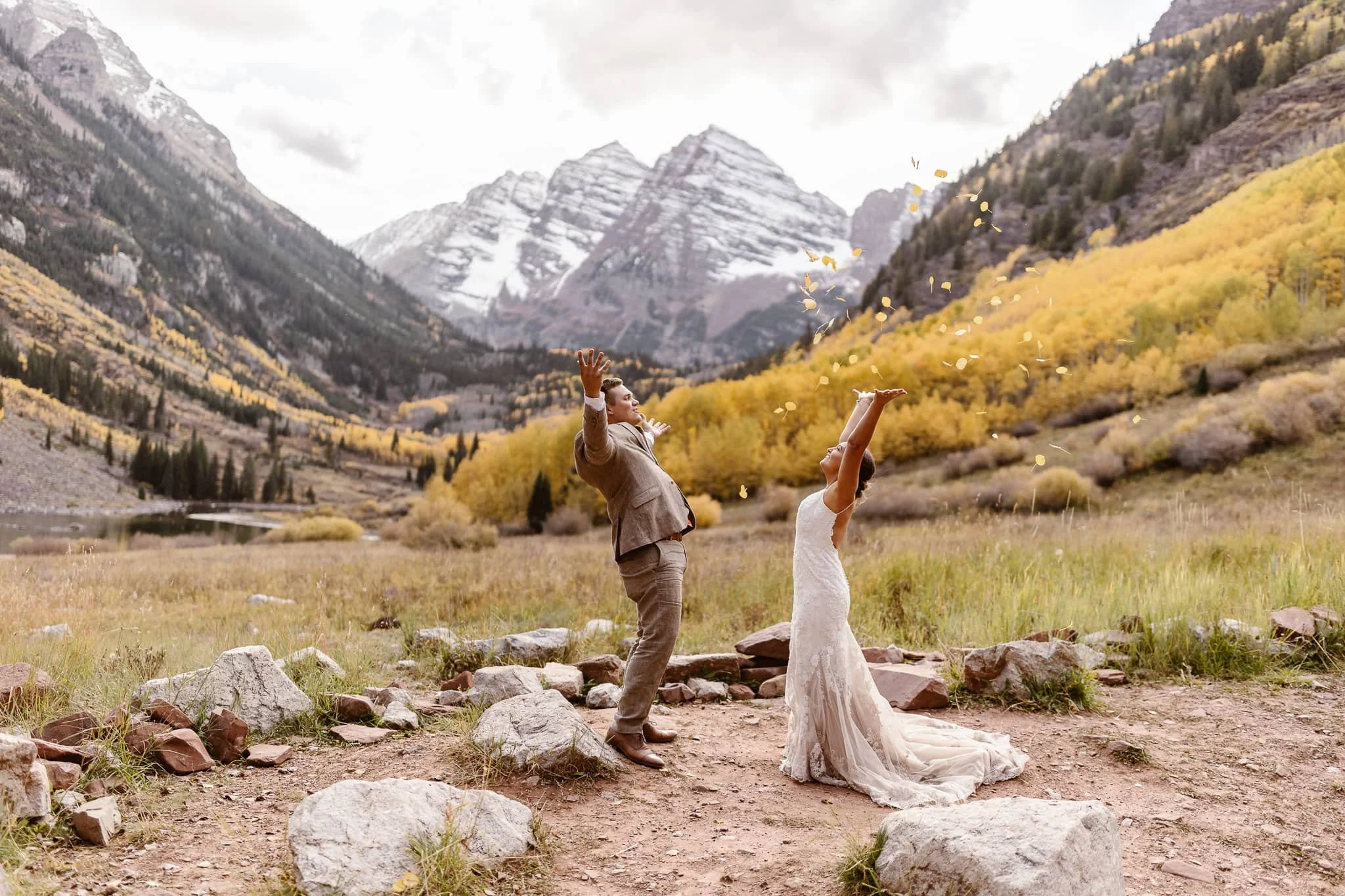 During a fall elopement at Maroon Bells, the bride and groom have their hands in the air as they throw yellow aspen tree leaves in celebration of their nuptials.