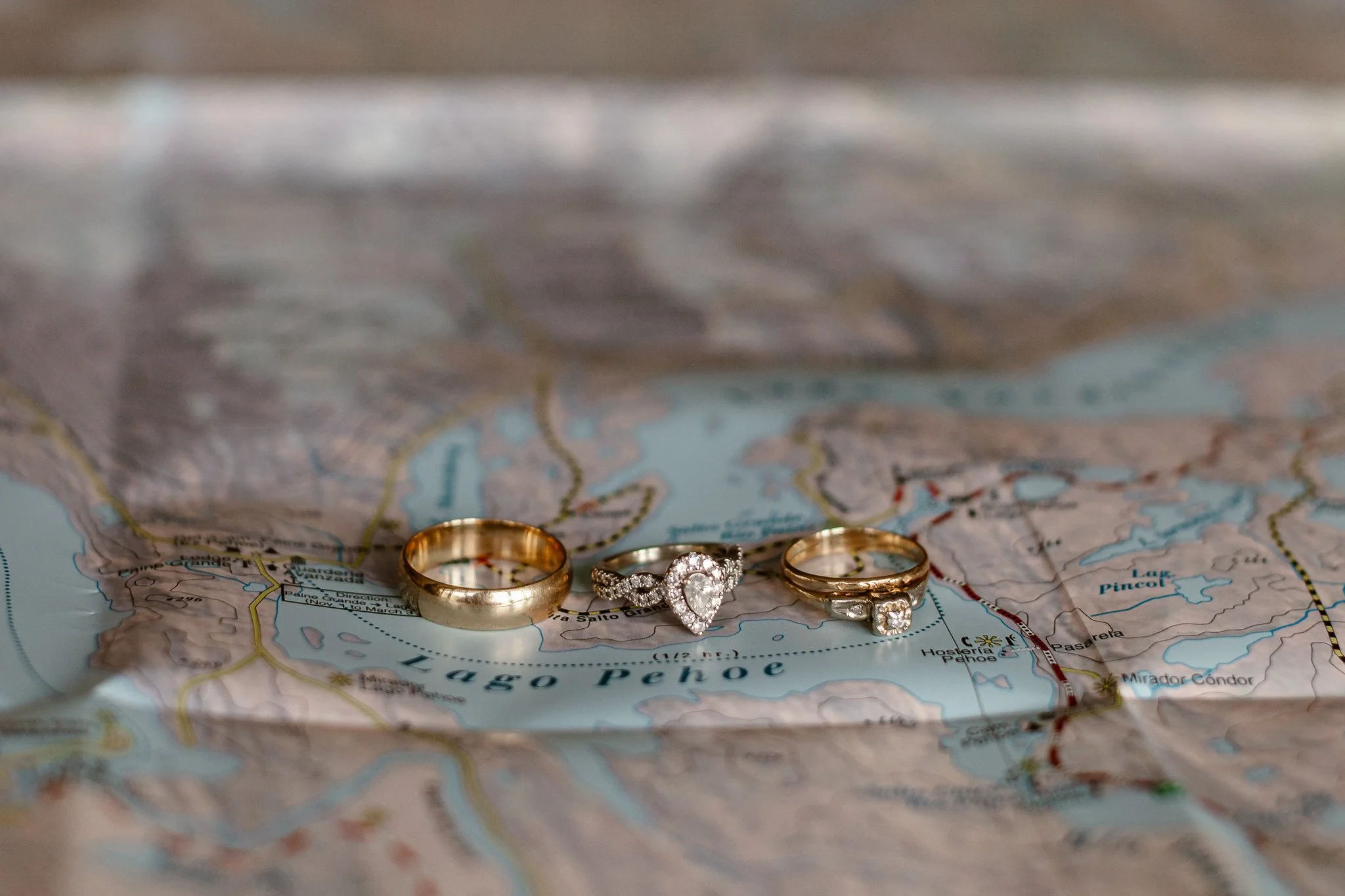 Three rings sitting on a map of Patagonia, starting with the groom's gold wedding band on the far left, the bride's pear-shaped engagement ring in the middle, and what appears to be a promise ring on the right.