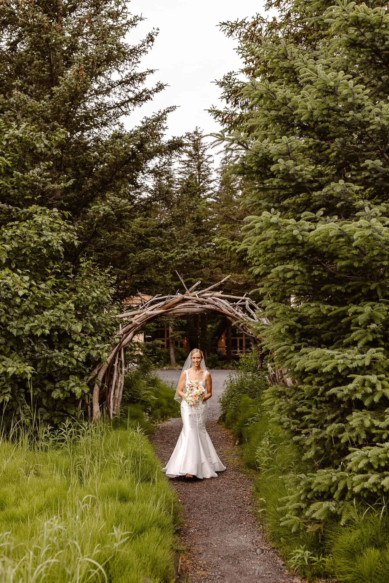 Walking to the first look under an arch made of broken branches, the glowing bride holds her pink, white, and peach bouquet.