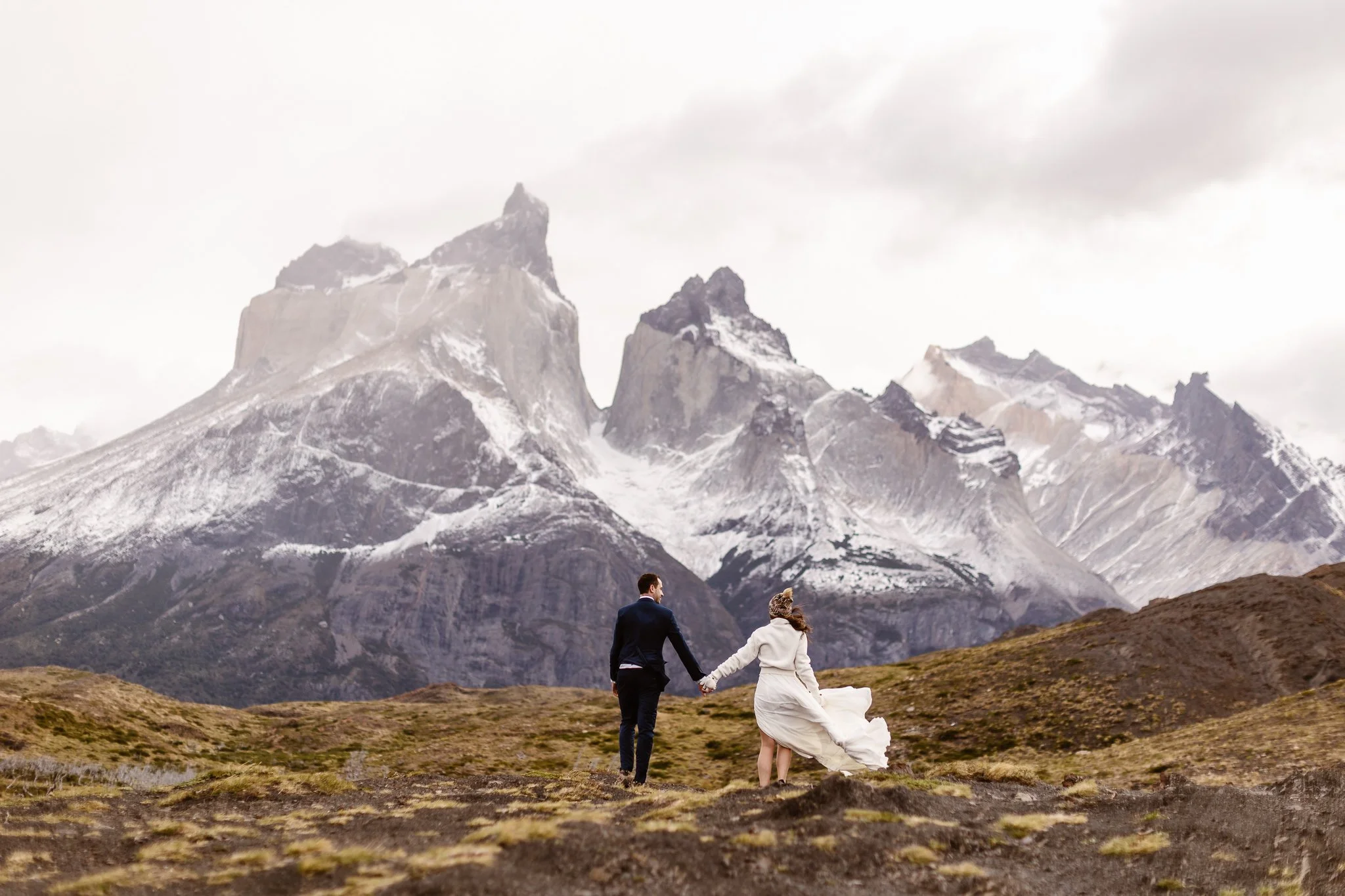 Newlyweds hold hands and face dramatic mountain peaks in Patagonia, Chile for their adventure elopement.