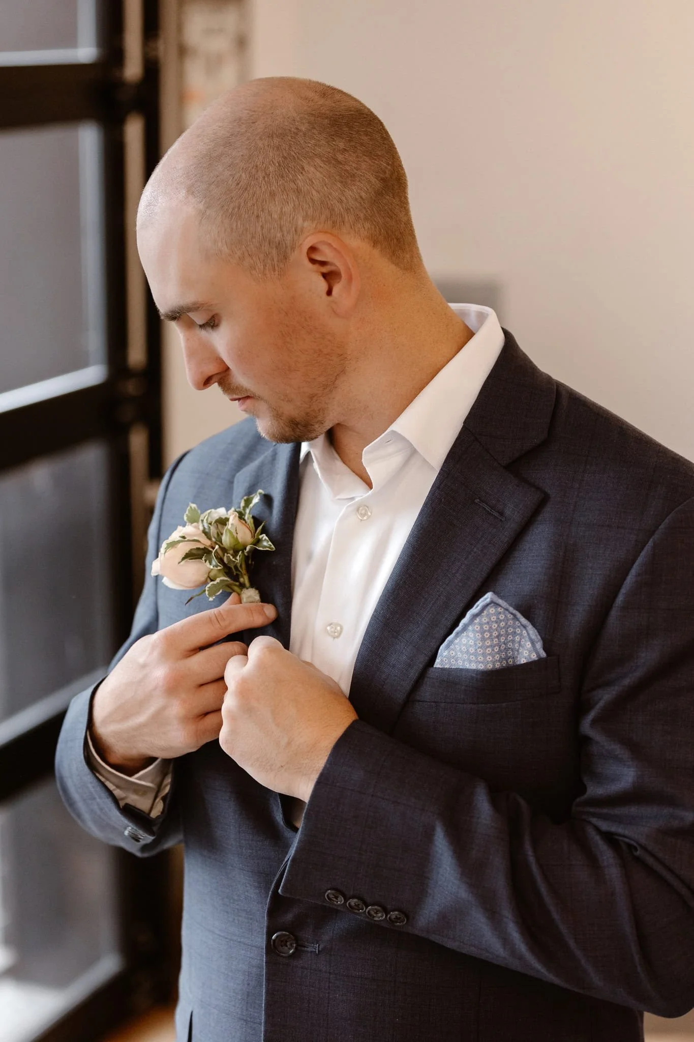 Adding his own final touches, the groom is seen getting ready, fitted in his dark blue suit and white shirt, adding his beach and green boutonniere to his lapel.