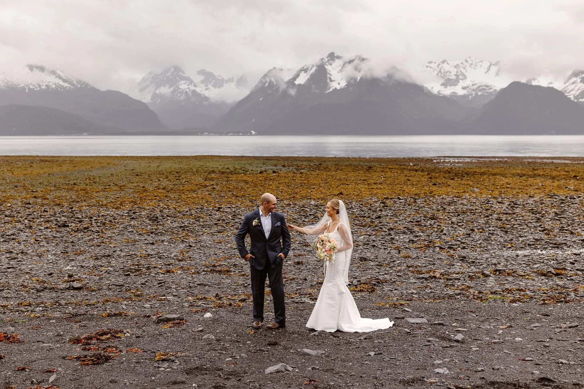 The reaction moment of their groom seeing his bride for the first time on their wedding day: he is smiling widely, almost in disbelief, as she gently touches his arm and smiles back, just as happily.