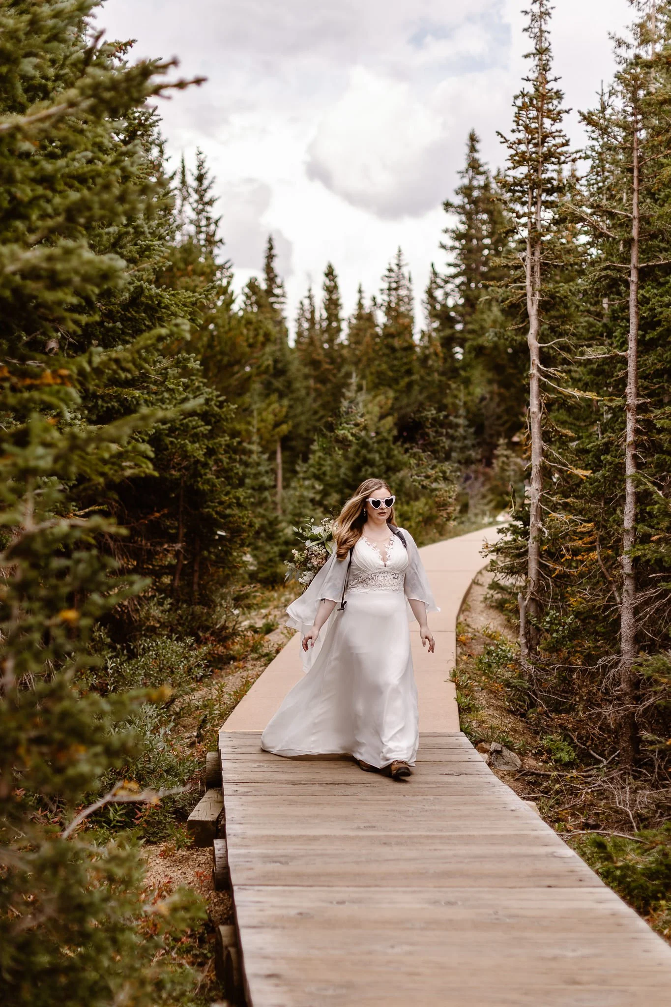 The bride, with her flowy sleeves and white heart sunglasses, struts down her wooden aisle through the olive green trees.