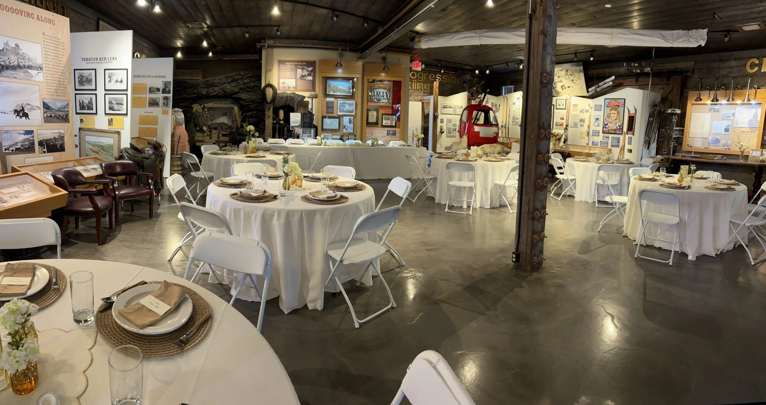 The inside of the Crested Butte Mountain Heritage Museum where a wedding reception is set up with round tables and white chairs around the room, with the exhibits all along with walls of the room.