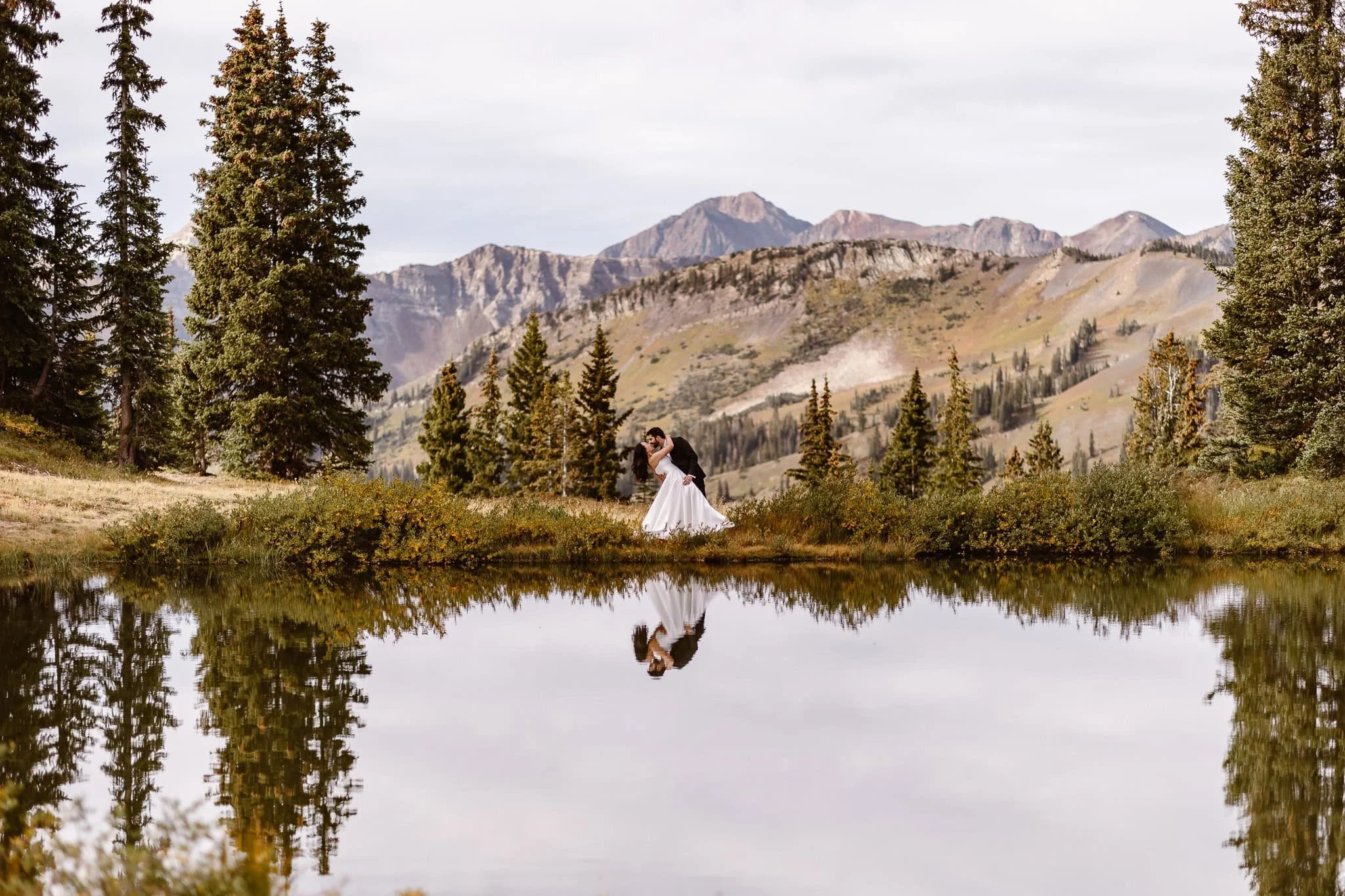 The next stop of this day of wedding portraits, the pair are at another still lake the reflects their image as the groom dips his partner in a romantic kiss.
