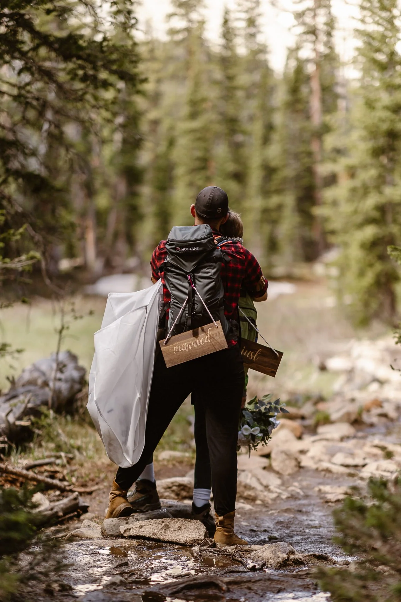 During their hike back from Lake Isabelle, the bride in groom stop for a moment on the rocky trail to be present and enjoy this moment, while wooden "just" and "married" signs hang from their backpacks.