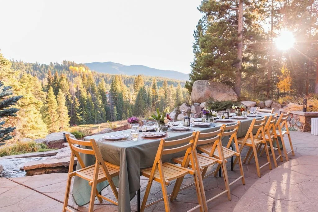 A fall wedding reception dinner table set up on the stone patio in the backyard of Star Mountain Home, complete with a long table covered with a blue tablecloth and wooden folding chairs.