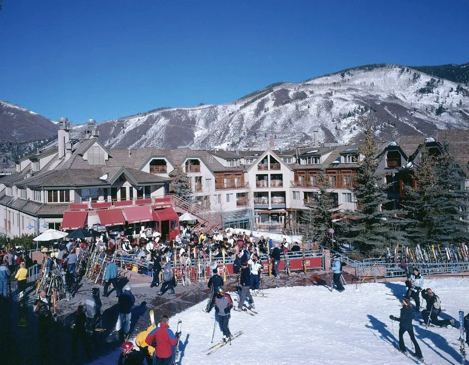 The exterior of Ajax Tavern in Aspen, showing where the pavement and the snow meet, this being the first place people can walk to after taking off their skis. The Image also shows the back patio of the restaurant and the rest of The Little Nell.