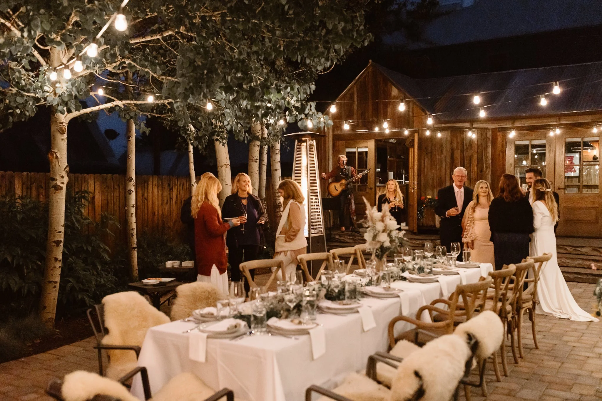 Backyard wedding reception at a private residence with a long table with white table cloth and formal dinner place settings