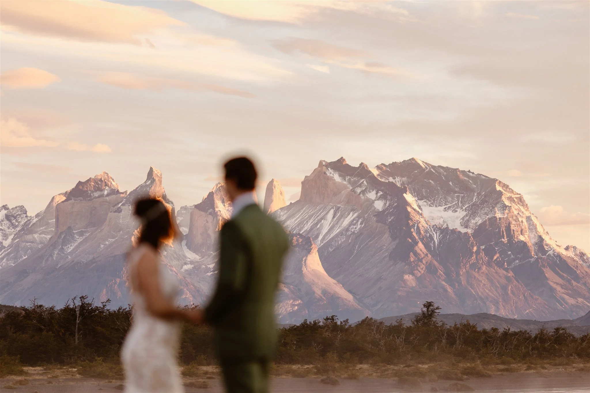 A shot of the couple holding hands and out-of-focus as they look off into the distant mountains behind them that absolutely shine during a pink sunrise haze.