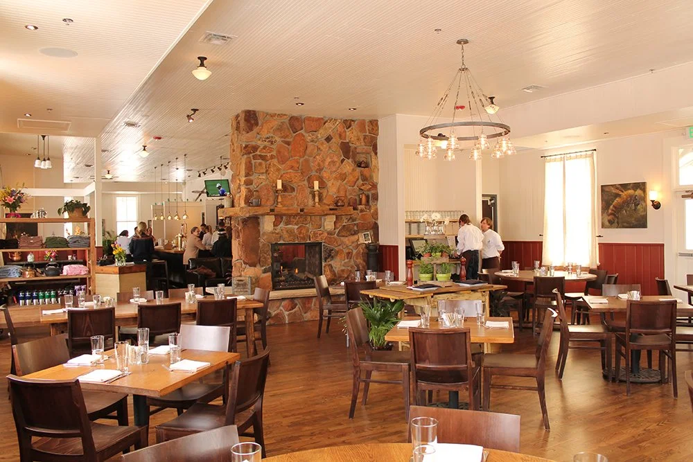 The interior of Chautauqua Dining Hall where the square wooden tables are set up throughout the space and stone fireplace takes center stage.