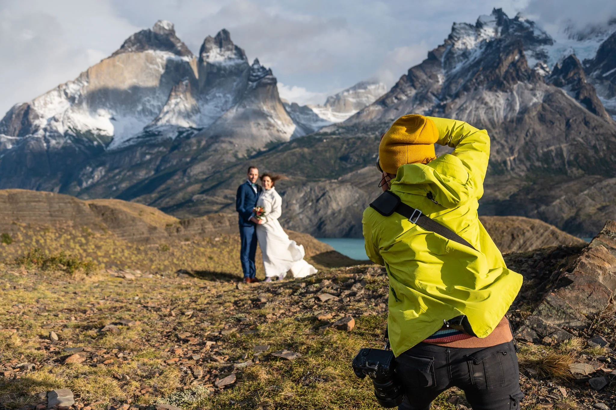 Elopement photographer, Andrea Enger, in a green jacket and yellow beanie take pictures of a bride and groom among dramatic rock formations during their Patagonia elopement