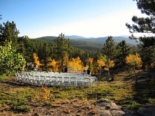 Rows of white foldable chairs arranged in a clearing surrounded by trees and mountains, making a perfect secluded ceremony space for an outdoor wedding.