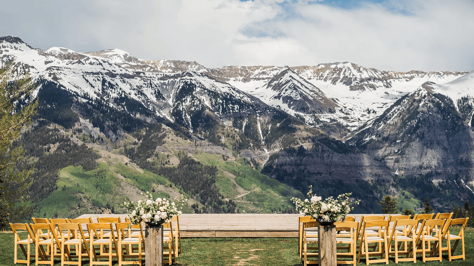 An overlook ceremony site that consists of just a wooden platform for the couple, and 2 rows of wooden chairs that face the couple and snow-dusted mountains that fill the background of the image.