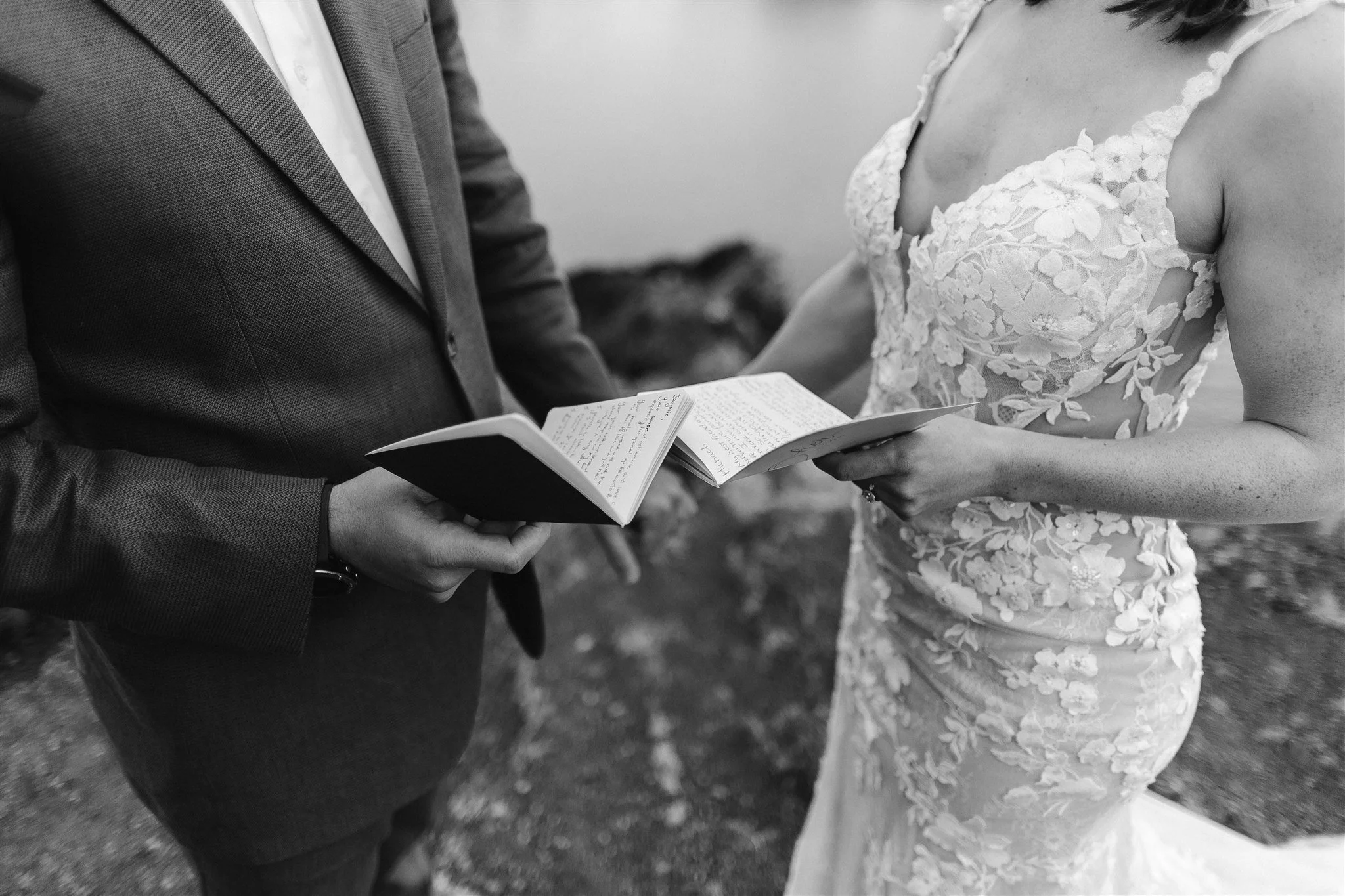 A close up shot of the couple's hands holding their vow books as they stand across each other by the lake. Here you can clearly see the beautiful floral details on the gown and their dazzling jewelry, like her sparkling ring and his glimmering watch.