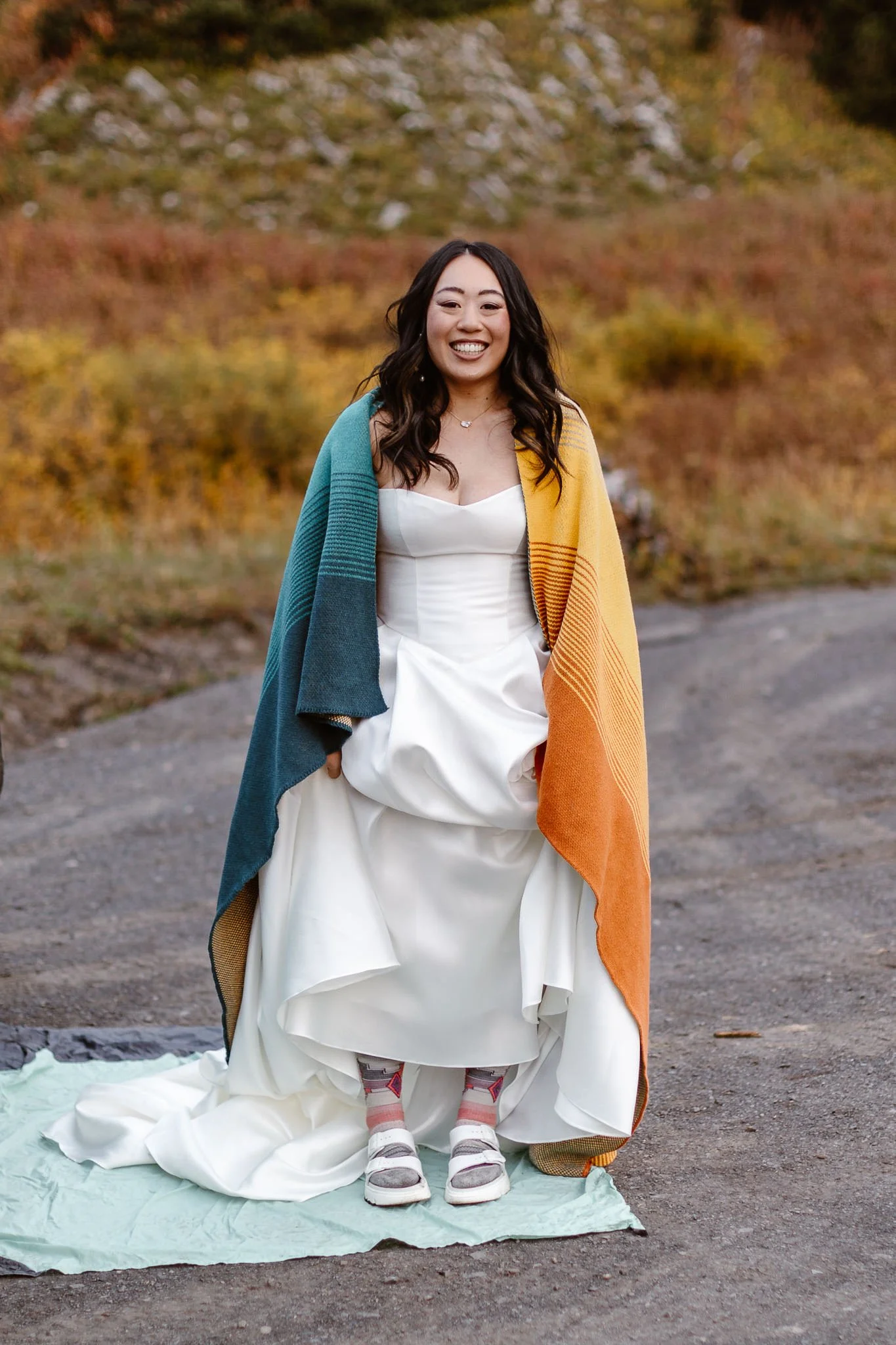 Standing on the other side of their car, the beaming bride holds her wedding dress up to show off her white sandals, as she's wrapped in a cozy blanket on this fall morning.