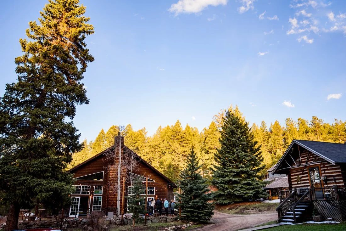 The exterior of some of the cabins and building at Meadow Creek Lodge. The building on the left has string lights on the outside and wedding guests talking on the lawn.