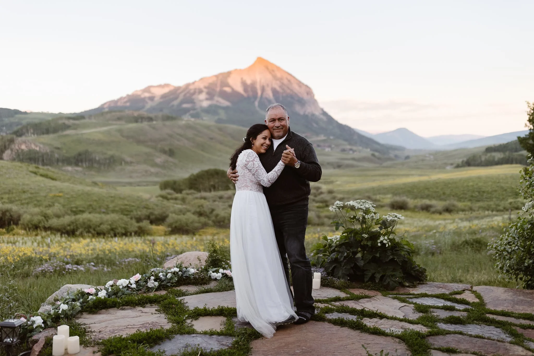 Father-daughter dance at an outdoor wedding venue as the sun sets on a pink mountain peak in the background