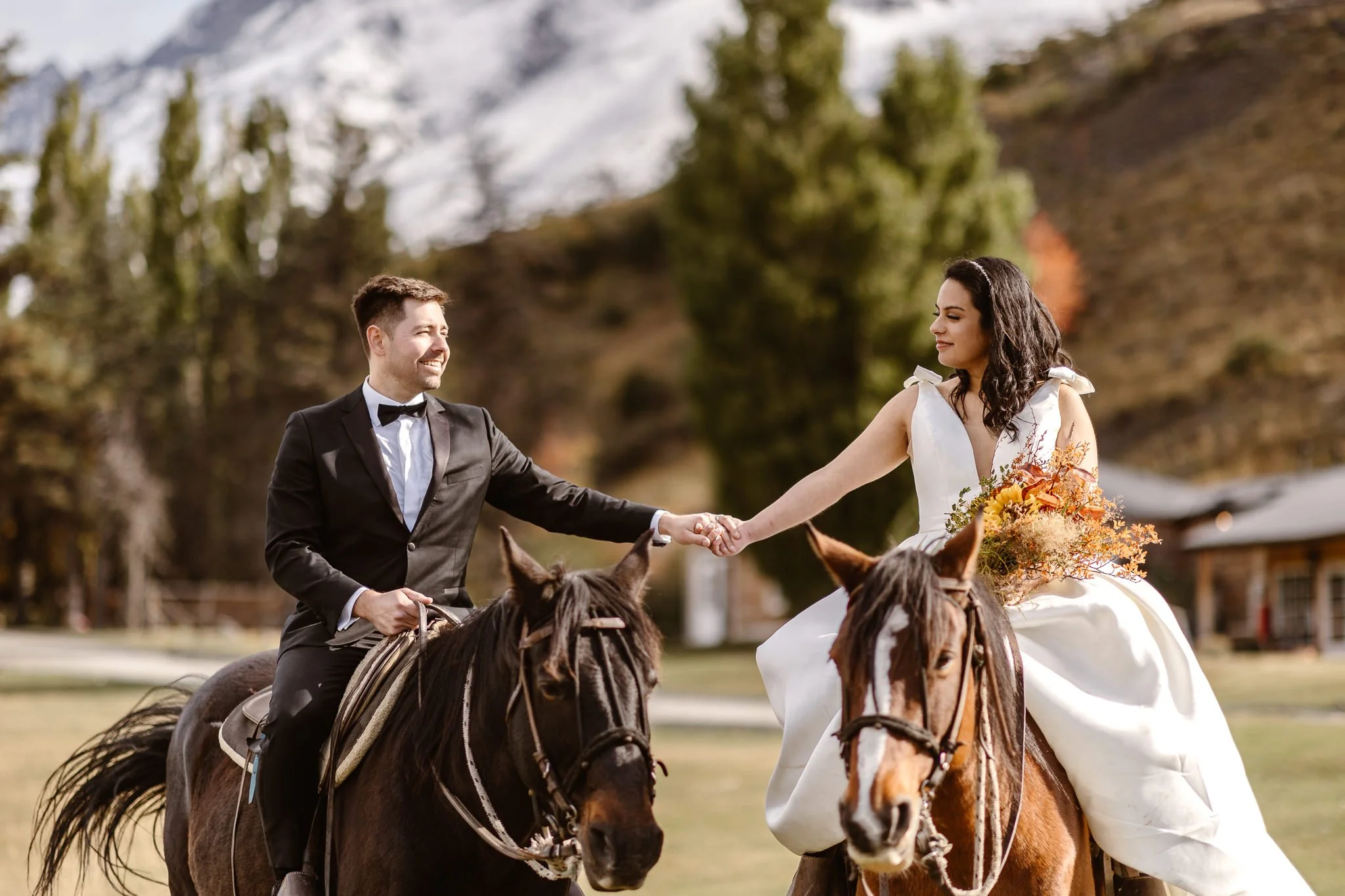 A bride and groom holding hands while on horseback during their Patagonia elopement. The bride on the right as she holds her bouquet in the other hand, and the groom is on the left, smiling at his new wife.