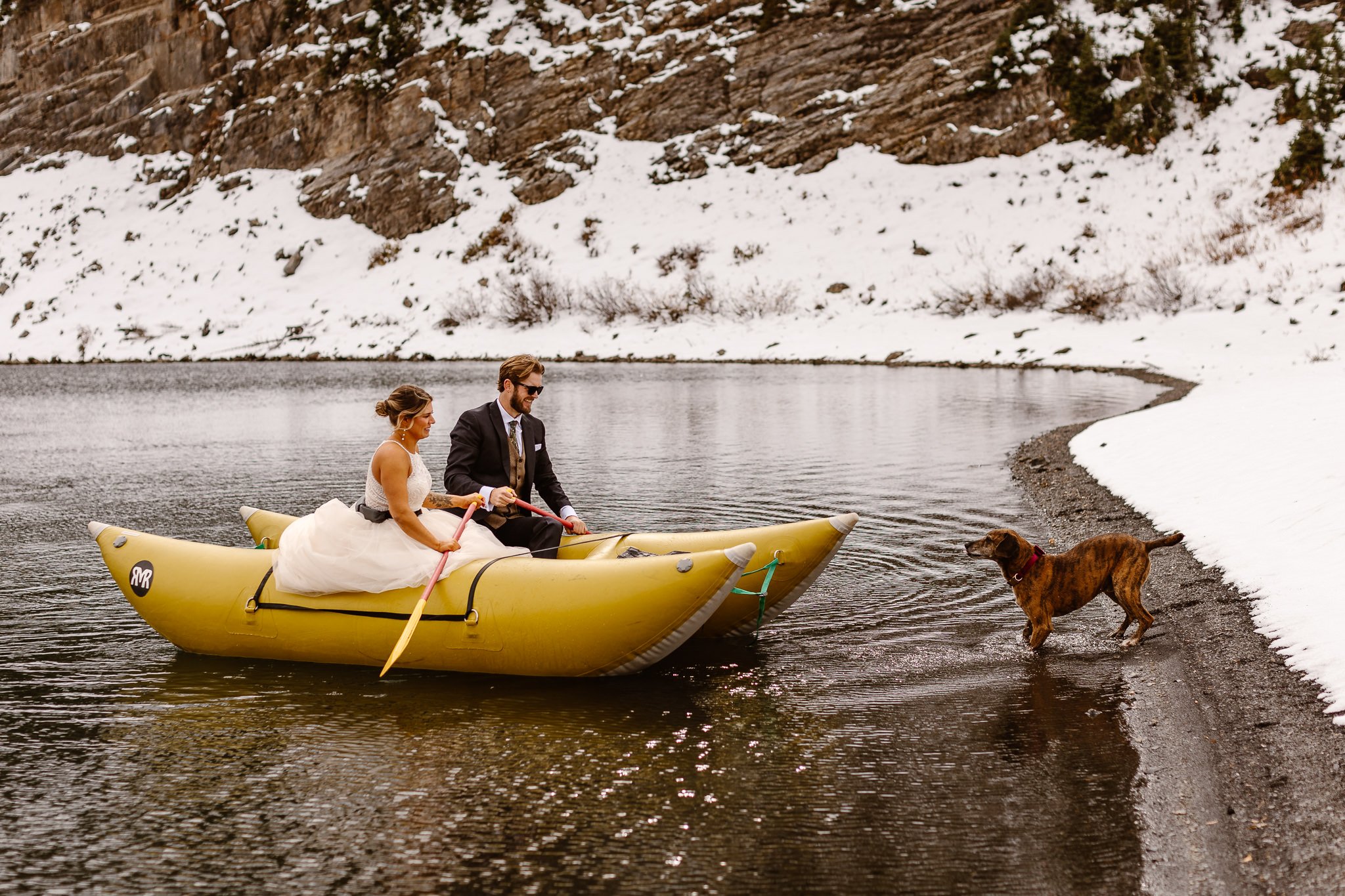 During a mid-October lake elopement in Crested Butte, the bride and groom meet their dog on the shore as they return from their celebratory canoe-ride in a large inflatable canoe. The ground is covered in snow but the joy overshadows any cold.