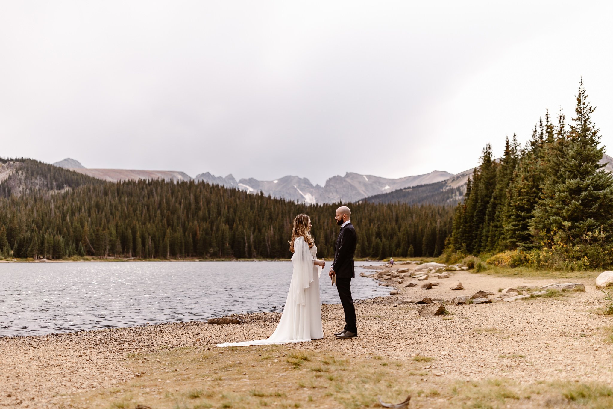Shot during their vows, there is a wide view of their elopement. The snow-speckled peaks behind them, the sea of forrest before the mountains, and the glimmering lake that is quietly listening.
