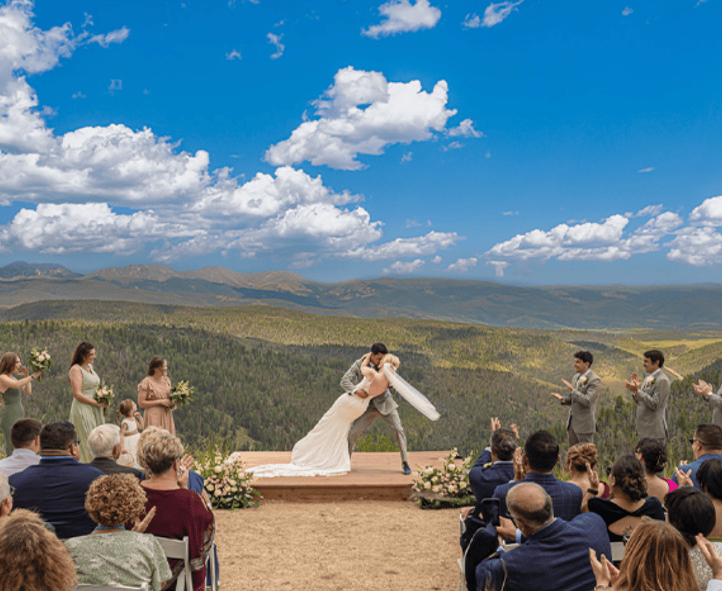 The open mountain space fills the entire background of this very simply wedding deck at Granby Ranch. The groom dips his bride during their first kiss as her veil blows to the right in the breeze, as they stand on a small wooden platform on the edge.