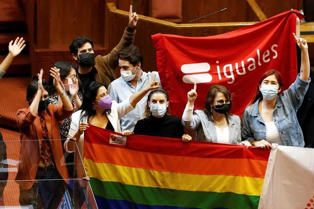 Masked supporters of marriage equality celebrate and hold a rainbow flag and a red flag reading "iguales" inside a courtroom