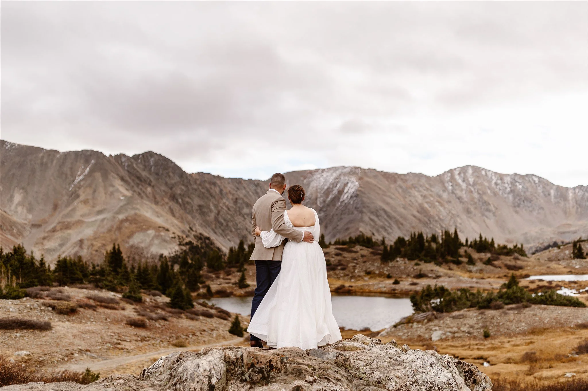 Standing on a large rock just outside of a serene lake in Breckenridge, these newlyweds are turned around with each other's hand on their back, soaking in the beauty of the dusty-brown mountains and glistening lake in the background.