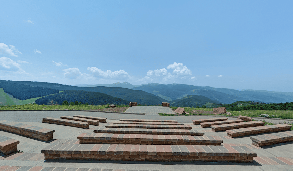 A cement and stone overlook that has built-in brick benches that are staggered, and a stone deck that overlooks lush mountains.