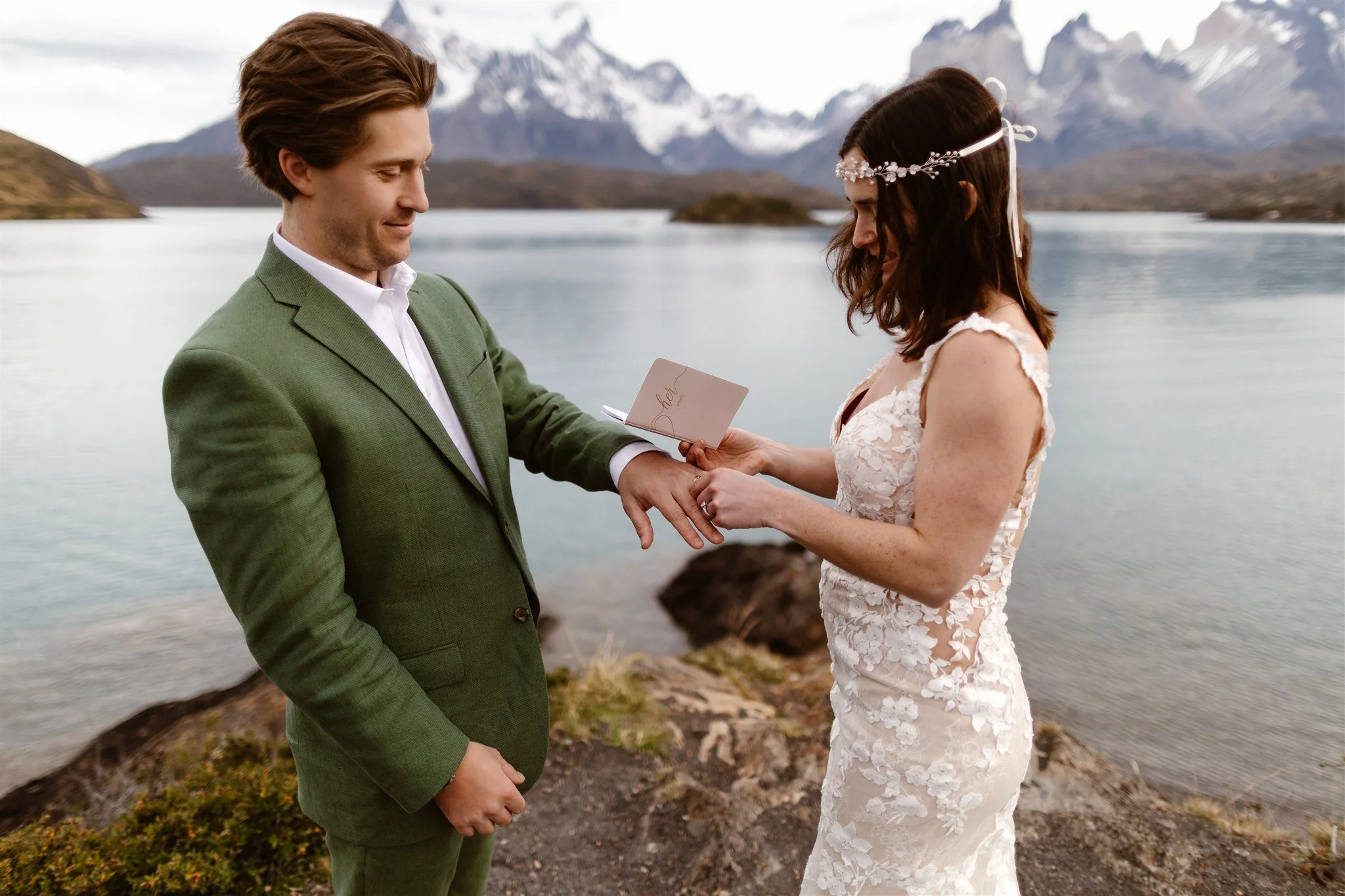 At the end of their intimate ceremony on the water, the bride is seen putting the ring on her groom's hand as the jagged grey mountains fill the sky behind them.