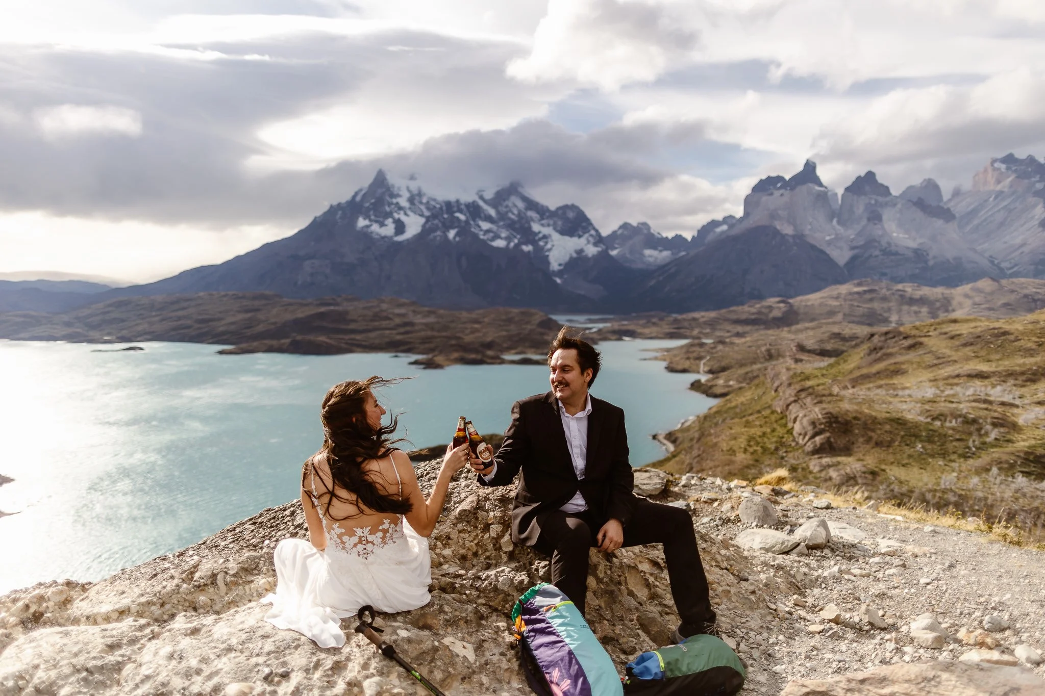 During the late afternoon in Torres del Paine, the bride and groom cheers with beer bottles while smiling sweetly at each other, enjoying this moment during their adventure elopement in Patagonia.