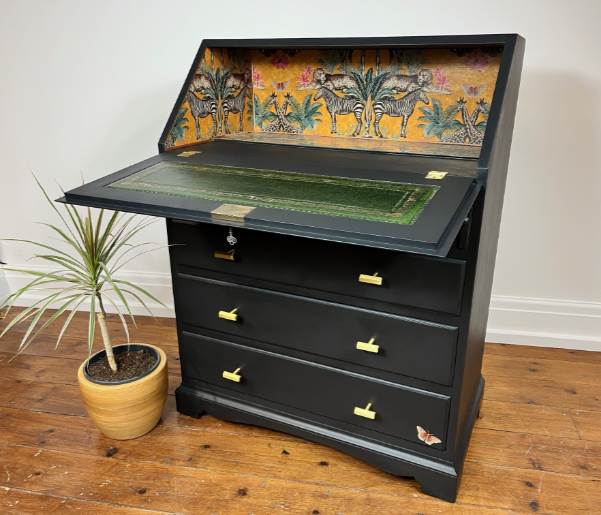 A black painted upcycled writing bureau with zebra and giraffe wallpaper on the interior