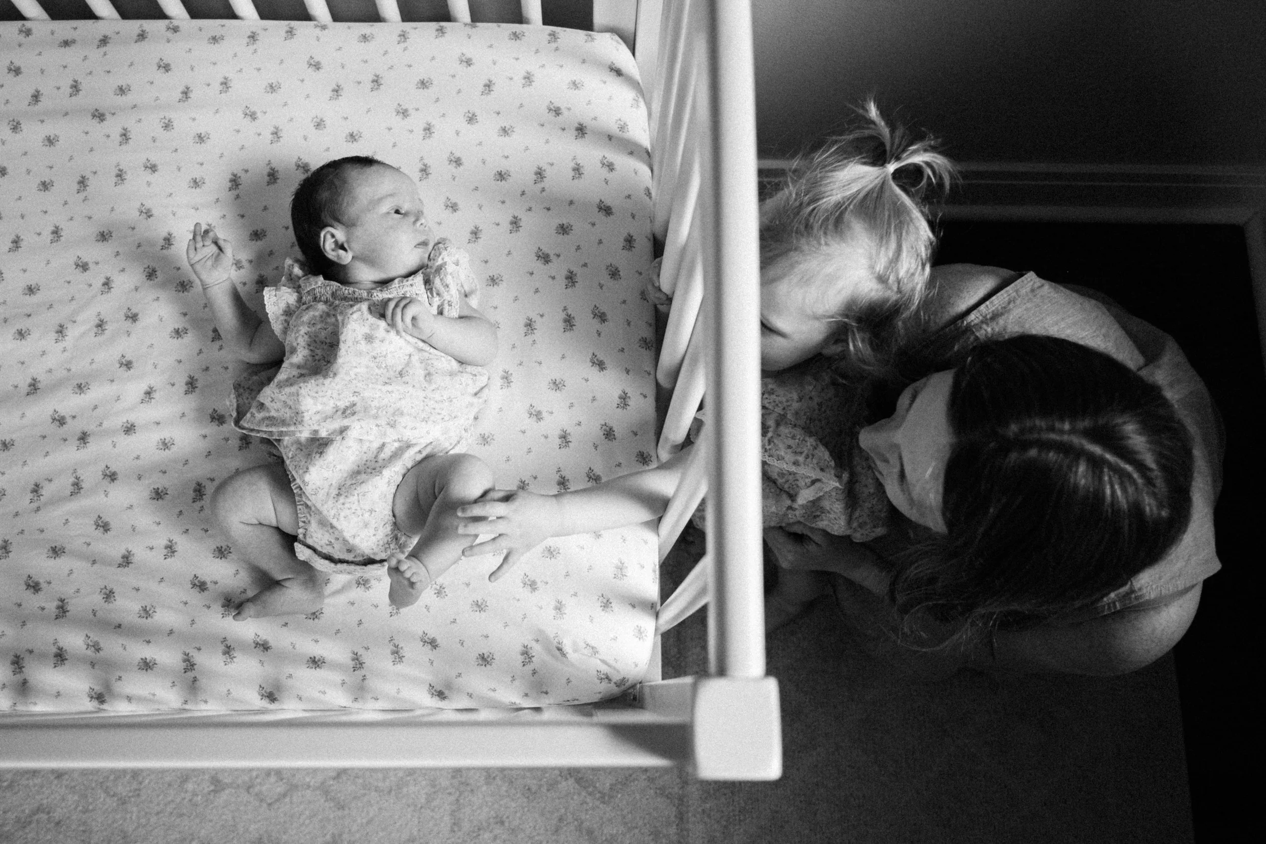 A black and white photo of a newborn baby lying in a crib and two women leaning over, sharing a tender moment.