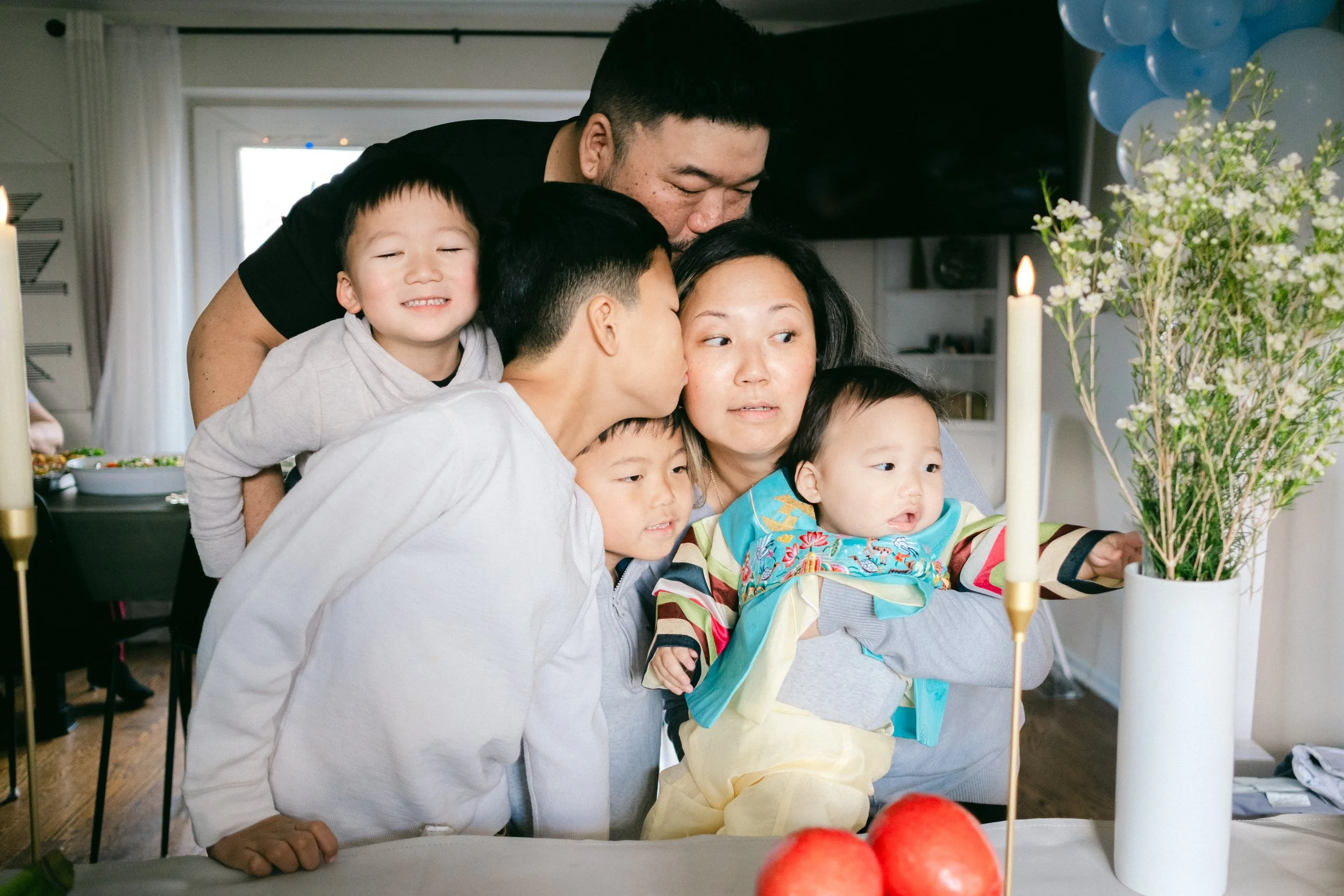 A family of five with two adults and three children sitting together in a living room, smiling and enjoying each other's company.