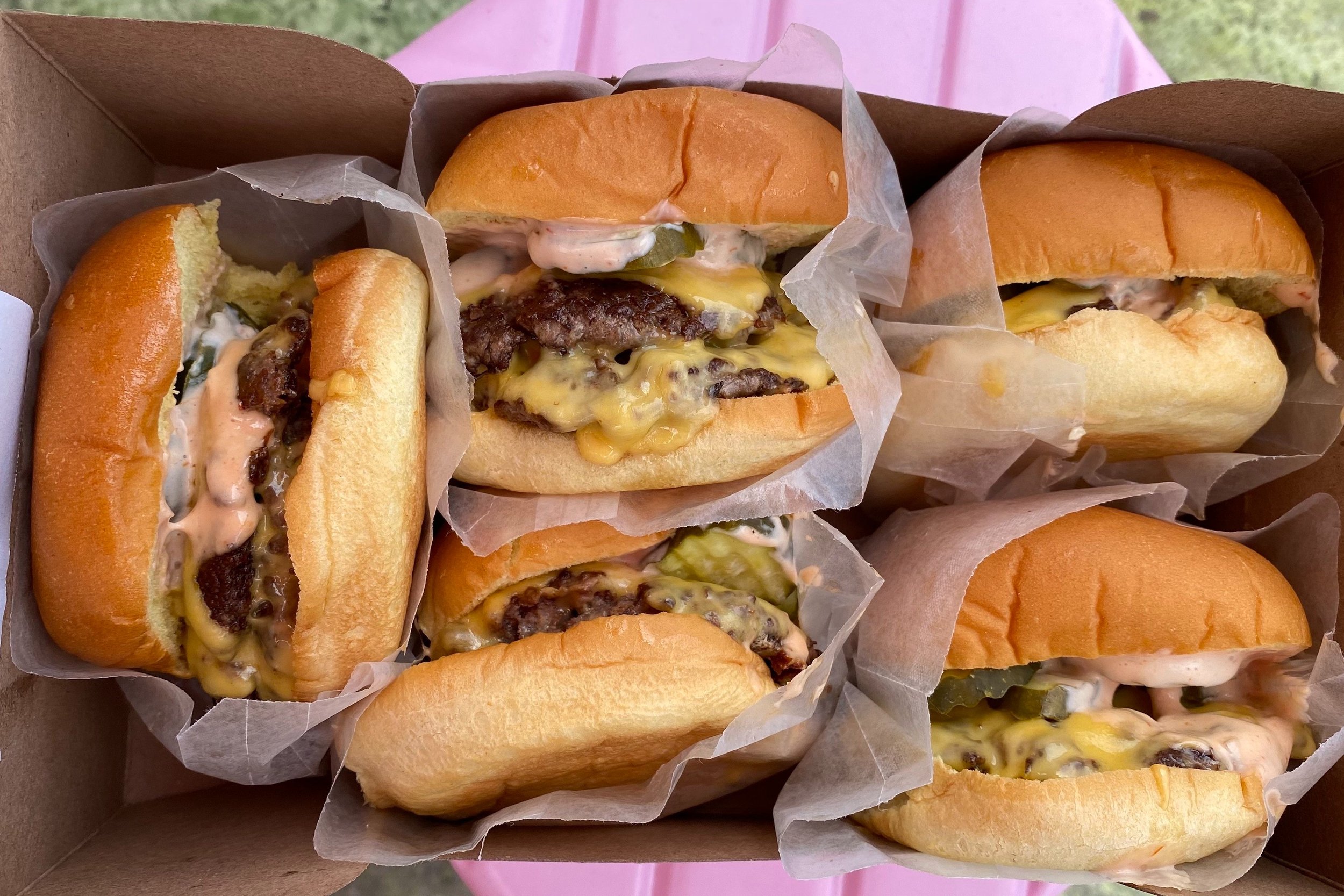  Five cheese burgers in a togo box on a pink stool 