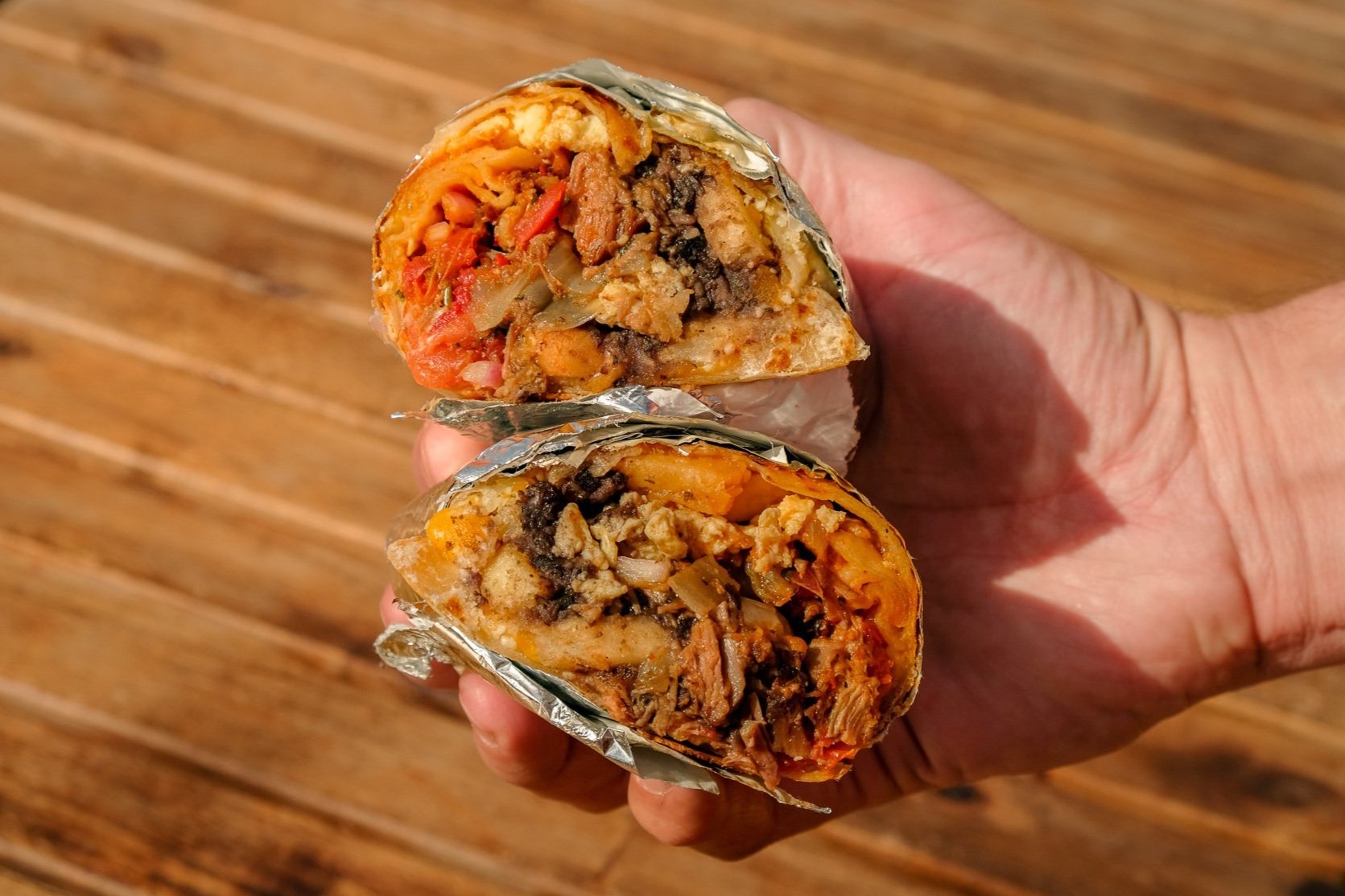  a hand holding a breakfast burrito cut in half to show the insides 