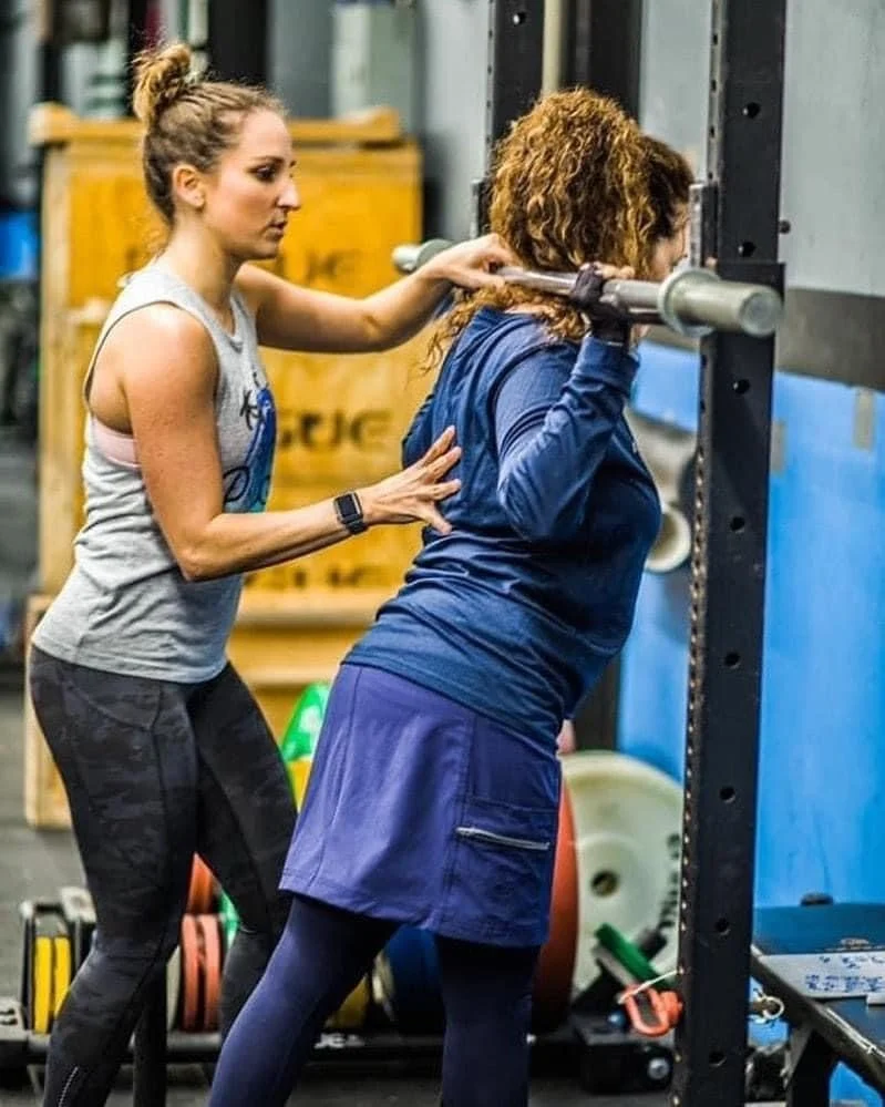 A trainer assisting a woman during a weightlifting exercise in a gym.