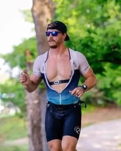 A man running outdoors wearing sunglasses, a cap, and athletic gear, with trees and greenery in the background.