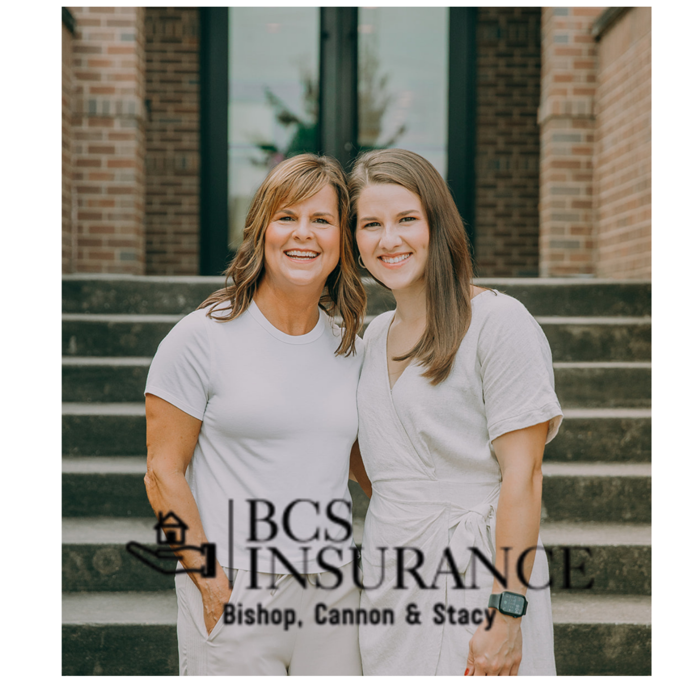 Two women smiling and standing on concrete stairs in front of a brick building with glass doors; one woman has short wavy hair and wears a white t-shirt, the other has long straight hair and wears a light dress; text overlay includes 'BCS INSURANCE,' 'Bishop, Cannon & Stacy'.
