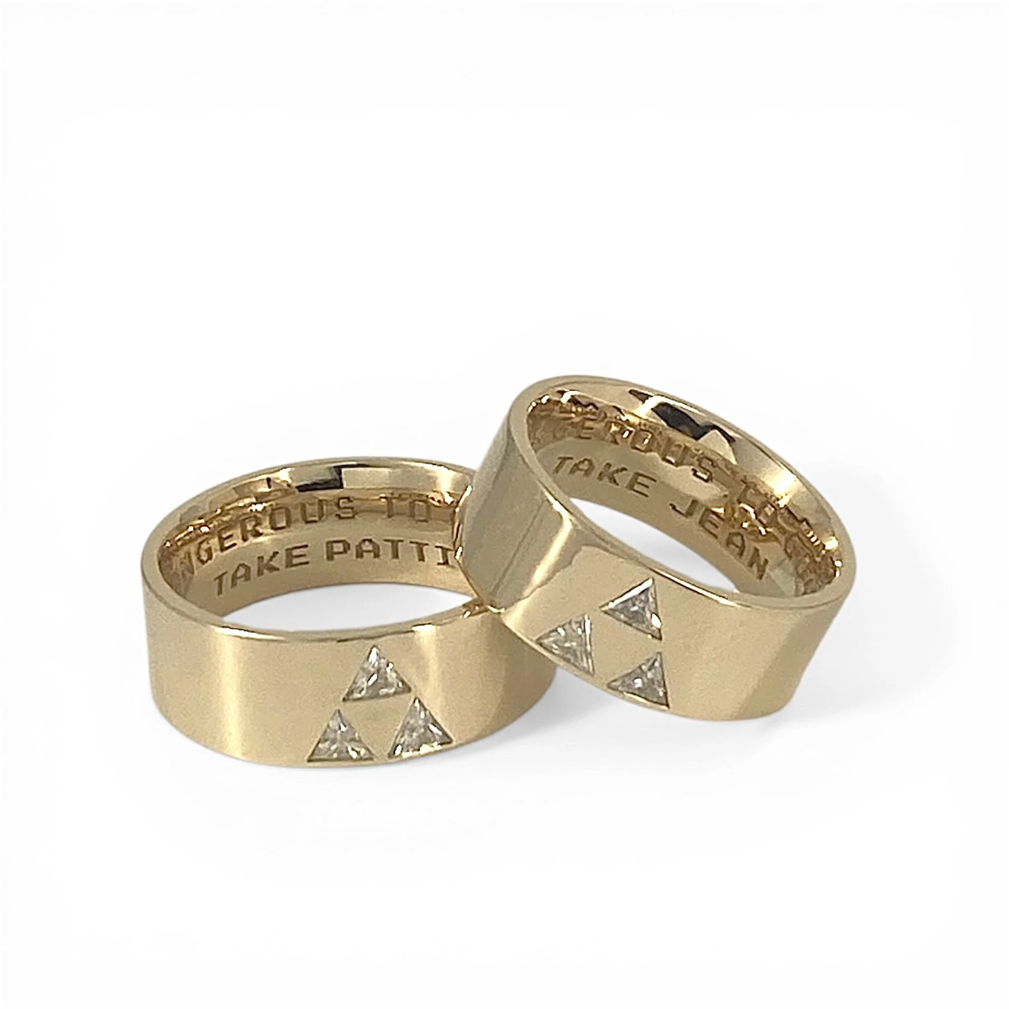 Close-up of several gold rings with engraved text, displayed against a plain white background.