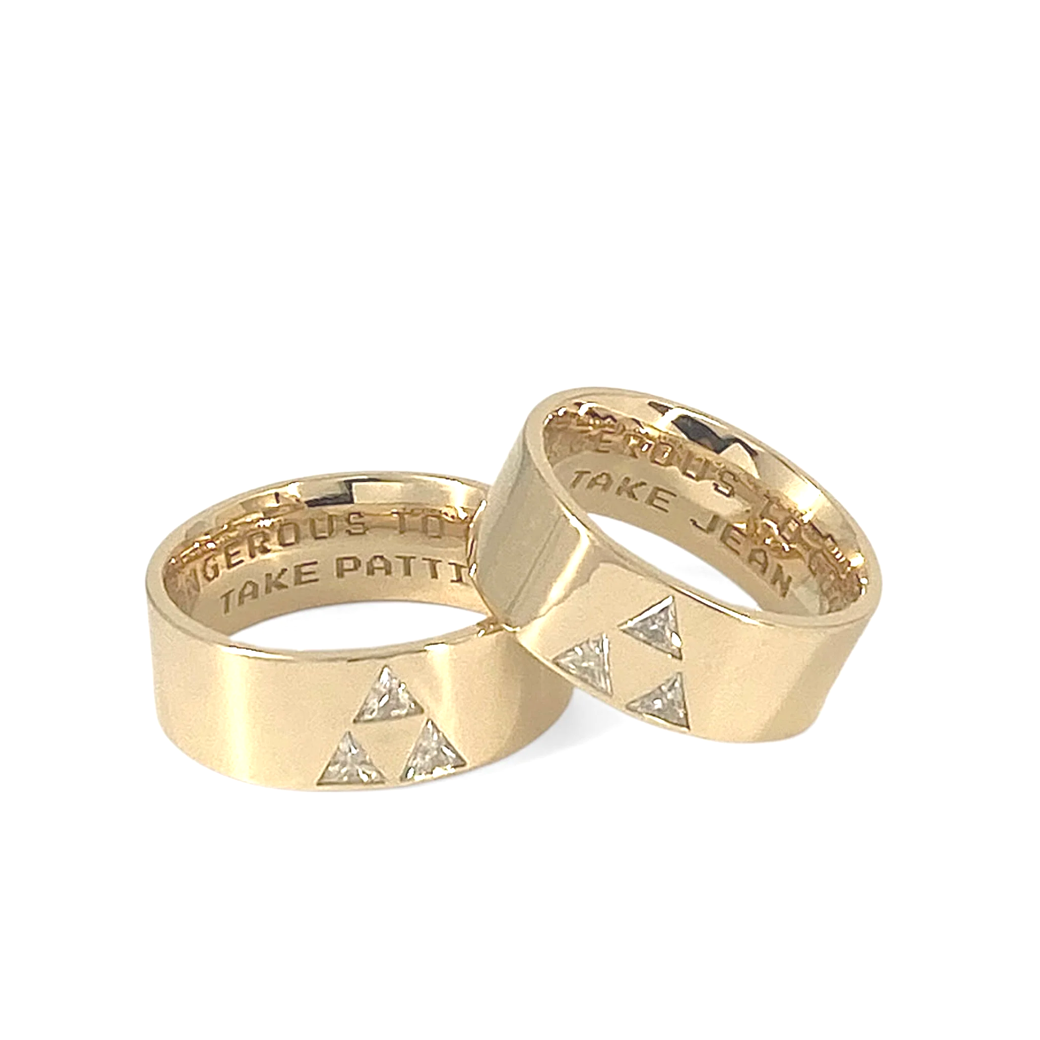 2 yellow 10karat yellow gold rings with 3 triangular cut Moissanite stones set in a triangular formation and inside engaving: IT'S DANGEROUS TO GO ALONE. TAKE PATTI AND TAKE JEAN. One ring resting on the other.