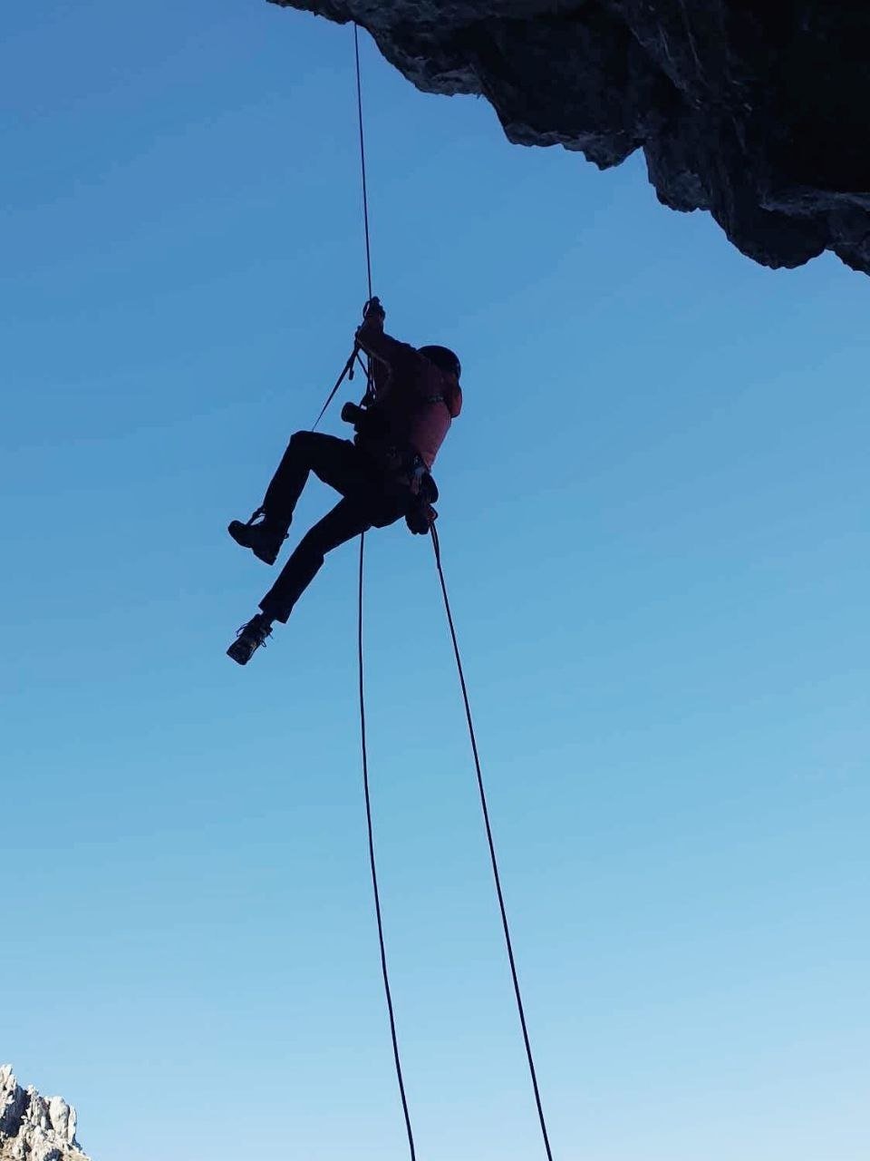 A person rappelling down a rocky cliff face with a clear blue sky in the background.