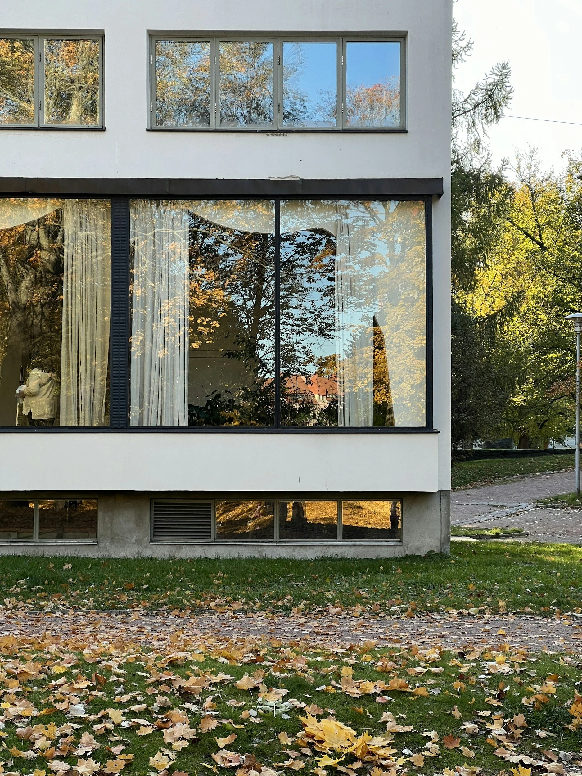 Image is of Alvar Aalto's house. Large windows reflective trees can be seen
