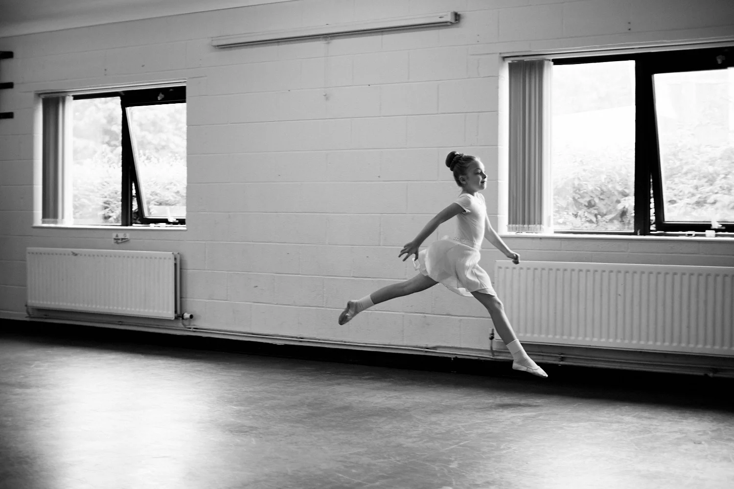 A young ballet dancer leaping through the air in black and white