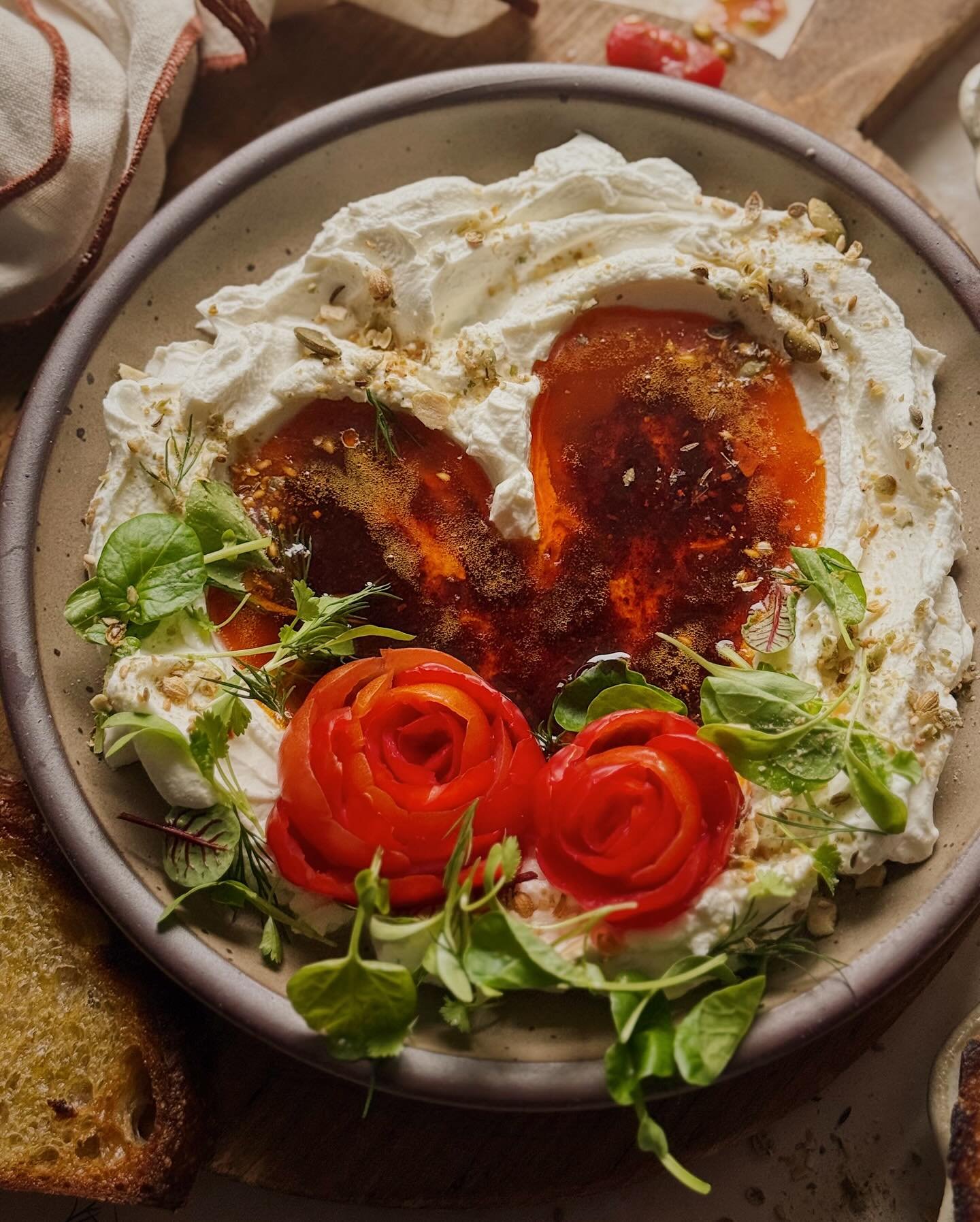 Labneh and a heart-shaped pool of chili butter, adorned with tomato roses, a medley of fresh herbs, and a sprinkle of pumpkin seed dukkah. Served with olive oil fried sourdough toasts for dipping.⁣
⁣
Here is a last-minute idea for a Valentine that yo