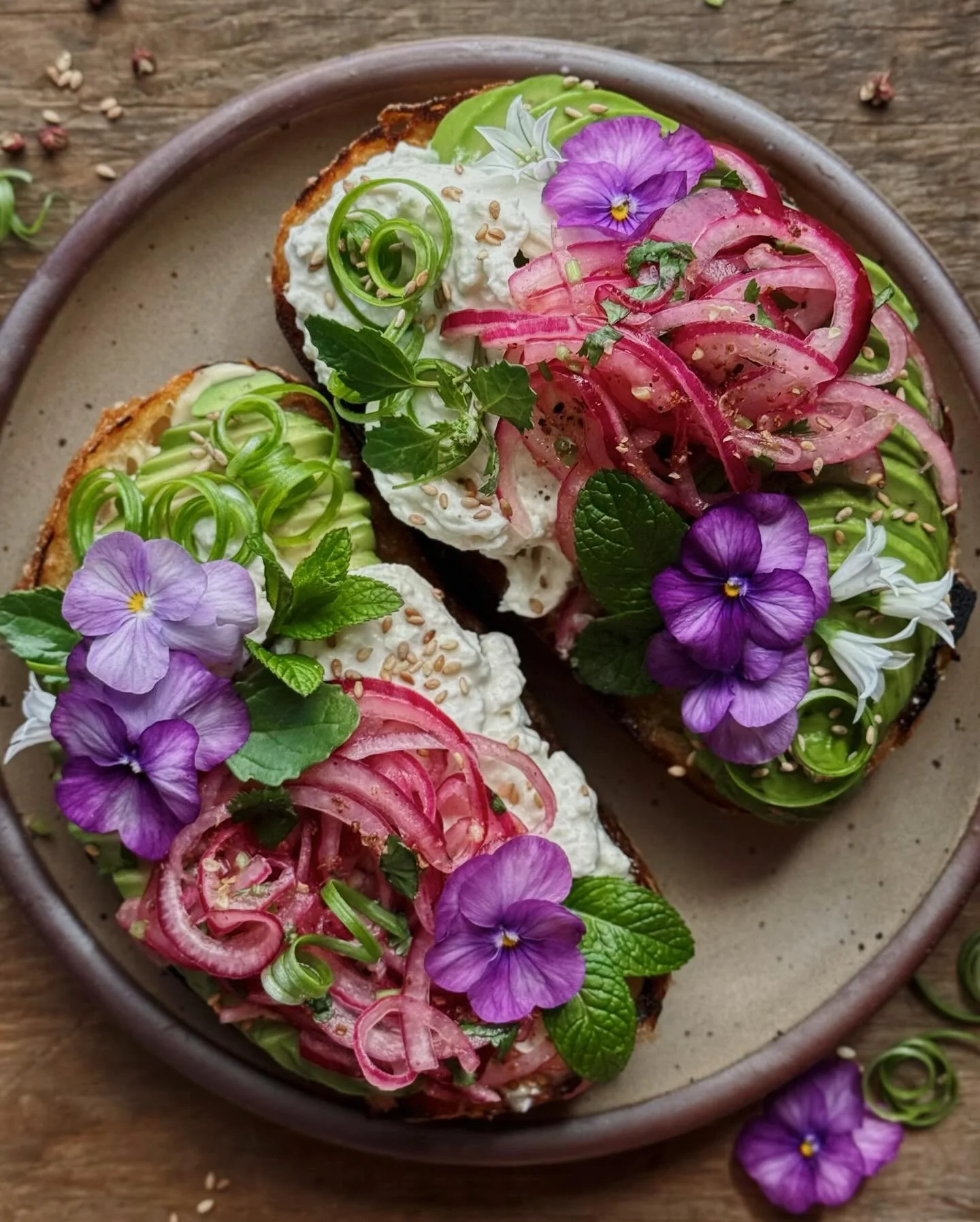 Avocado toasts with kewpie mayo, burrata, fresh herbs, scallions, sesame seeds, and tingly pickle-y onions. The flowers are violas and three-cornered leek.⁣
⁣
I have seen a lot of videos for sumac onions on my explore page lately and I think that got