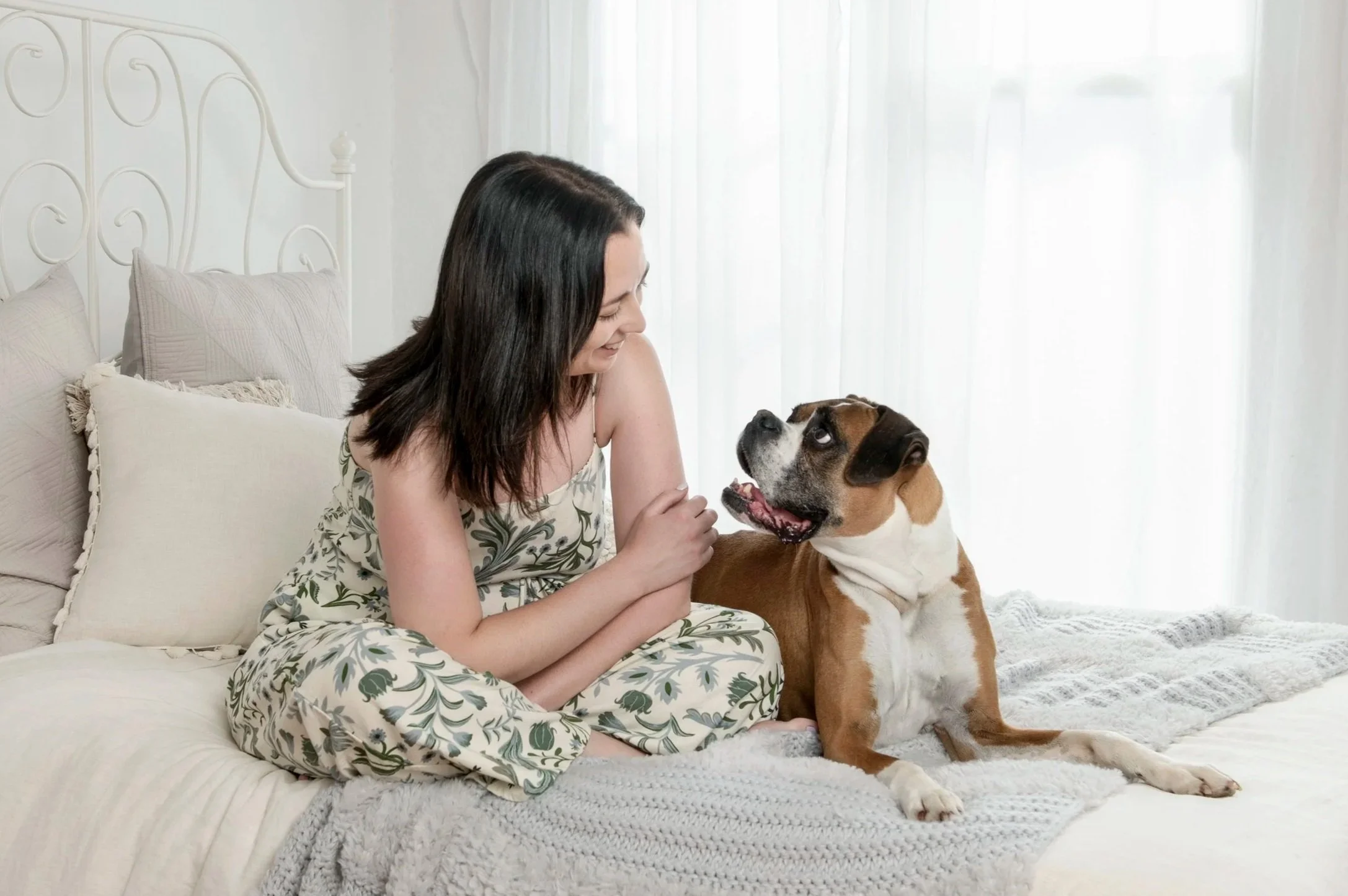 Woman sitting on a bed gazing at her boxer dog during a Sydney pet and owner photography session