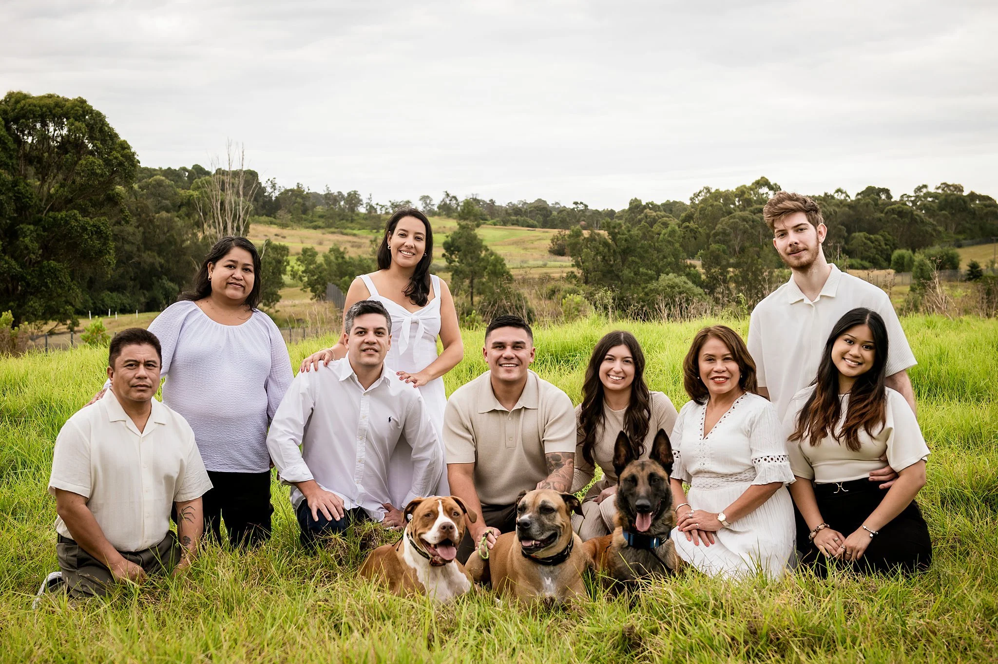 Extended family group in a grassy field with their three dogs during an outdoor family photography session in Sydney