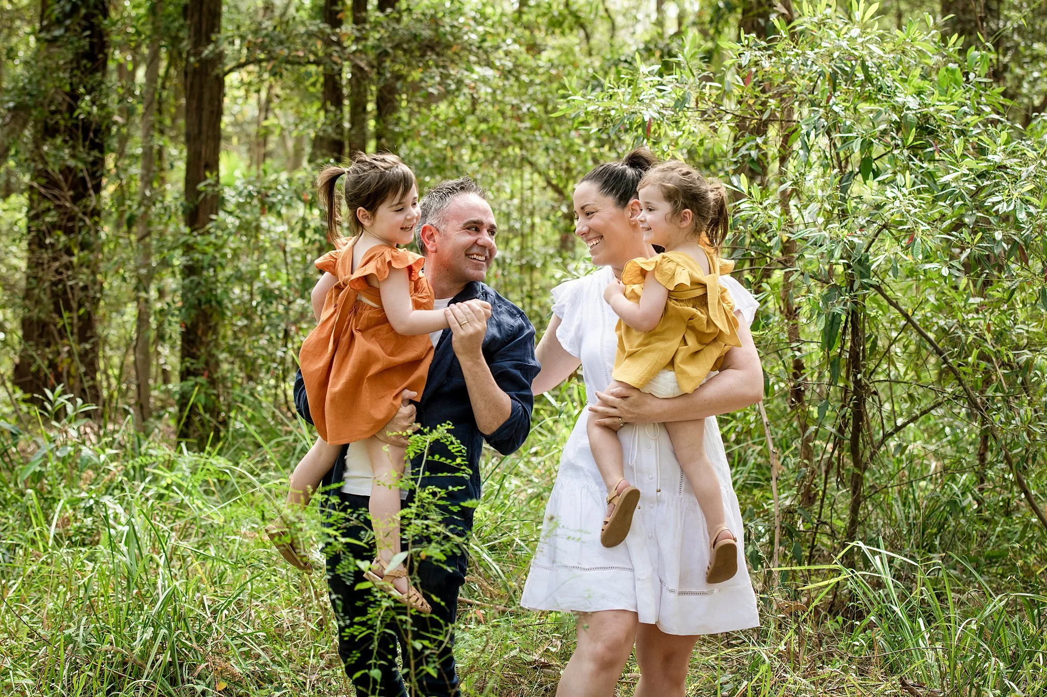 Parents carrying their two young daughters through bushland during an outdoor family photography session in Sydney
