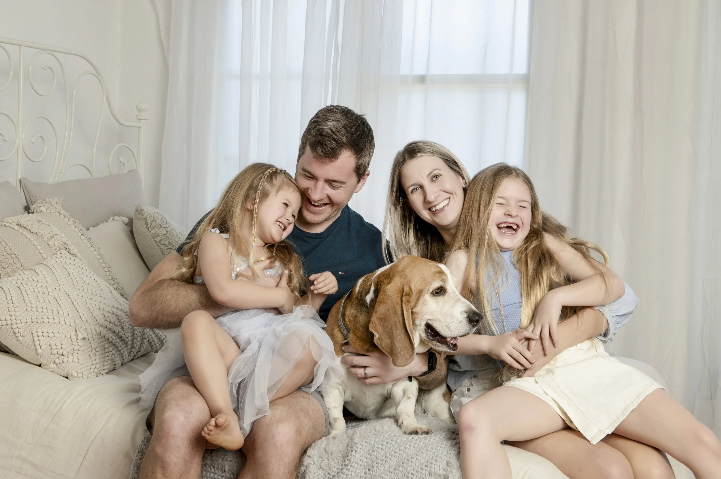 Sydney family of four laughing on a bed with their beagle sitting in the centre, soft natural studio light